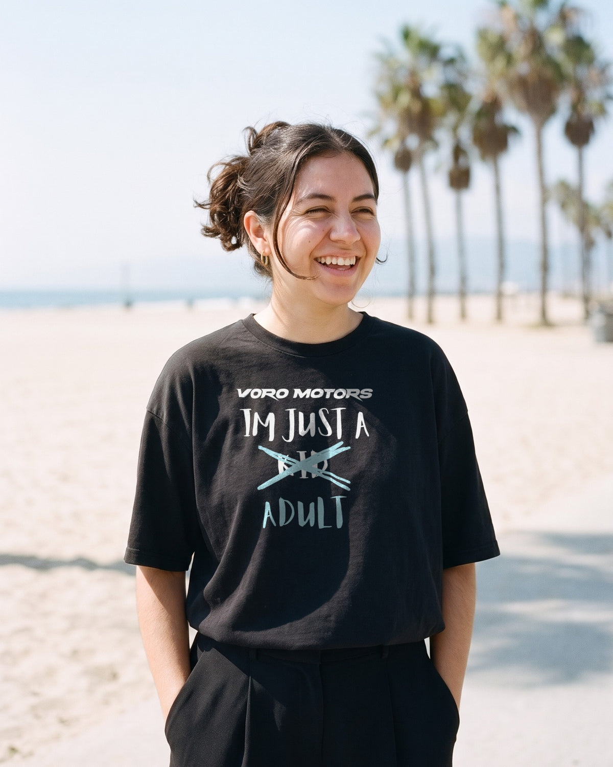 Woman laughing in the I'm Just a Kid Adult oversized tee on a beach boardwalk