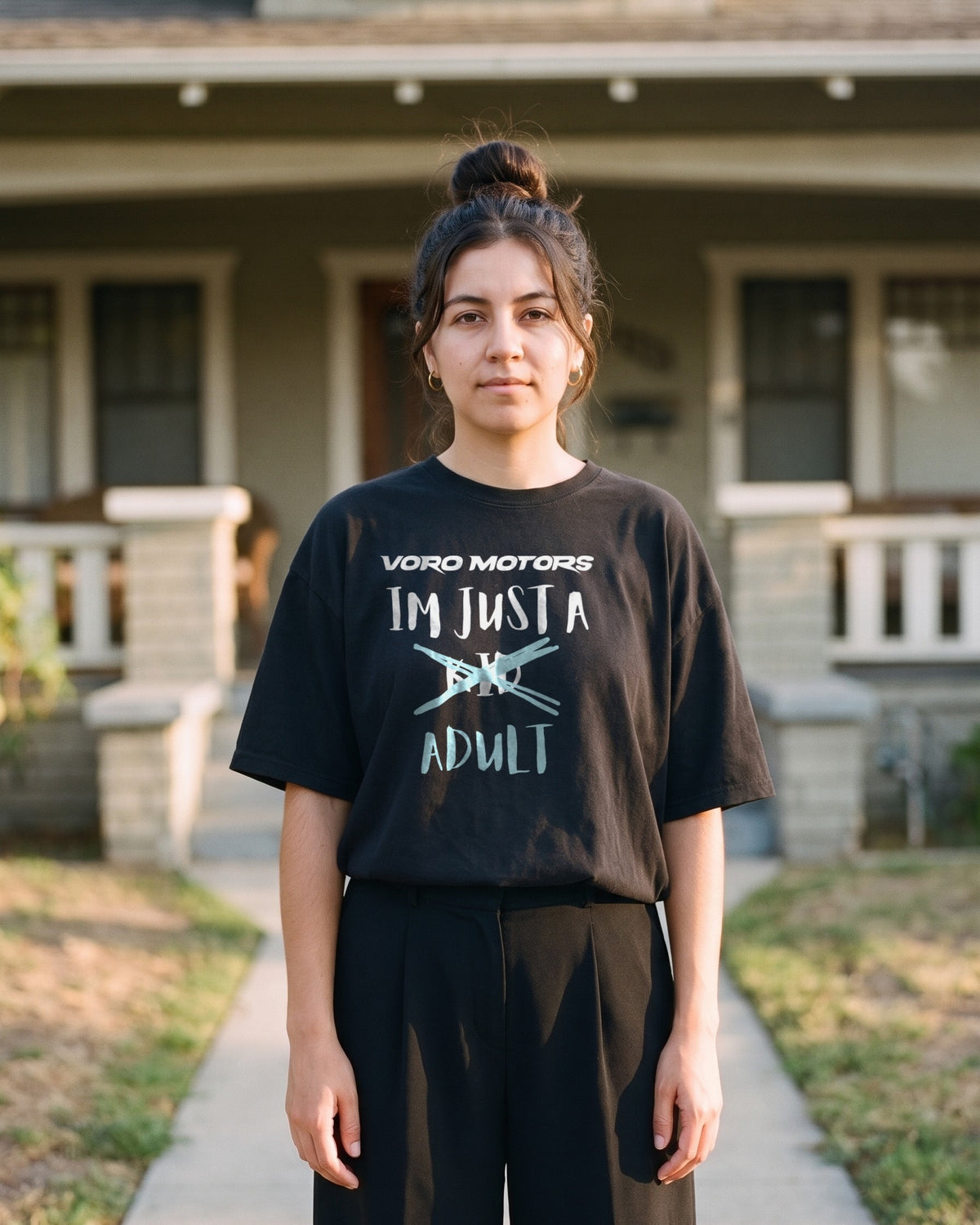 Woman in the I'm Just a Kid Adult oversized tee on the front walk of a Pasadena Craftsman house