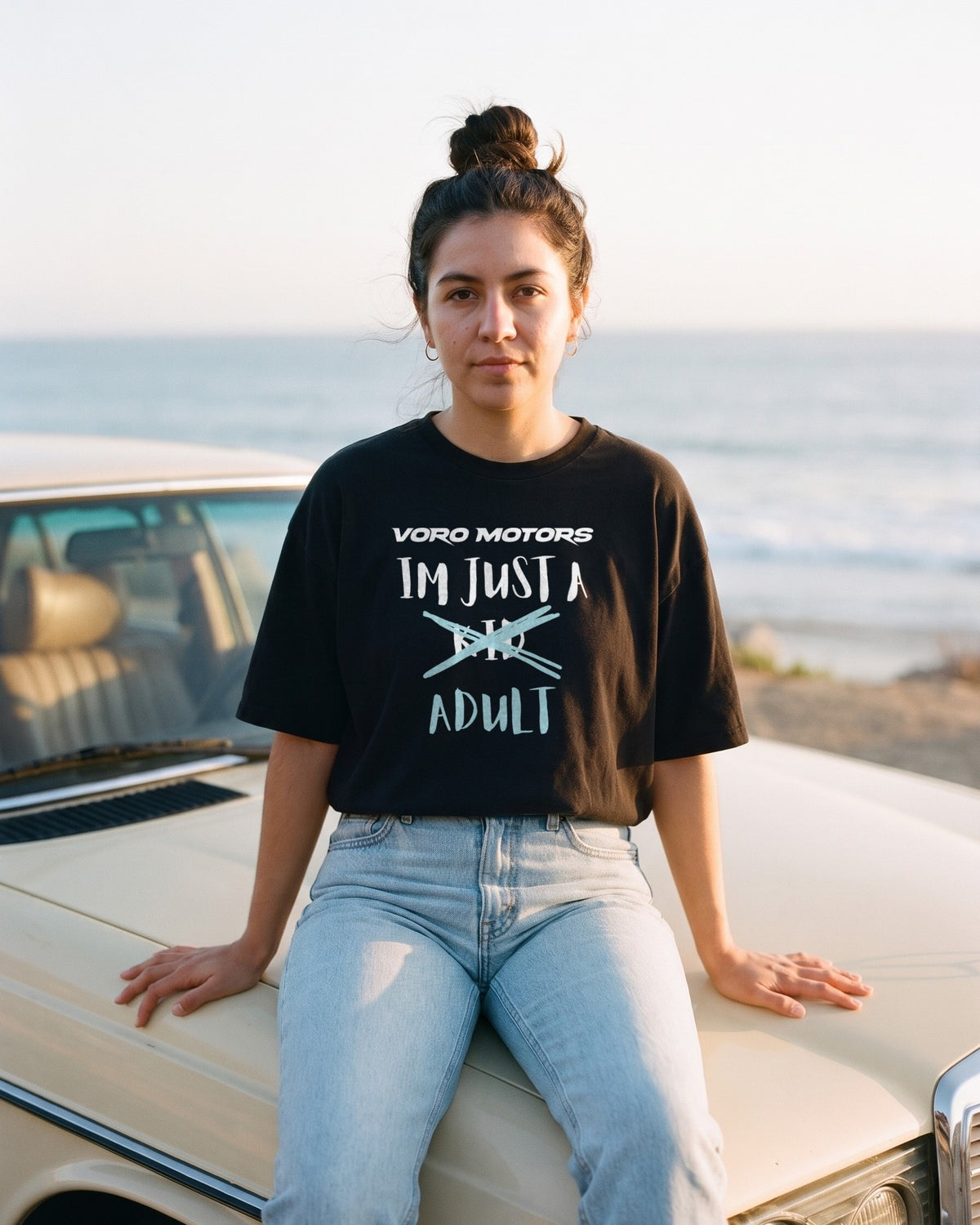 Woman in the I'm Just a Kid Adult tee sitting on a classic car hood in Malibu