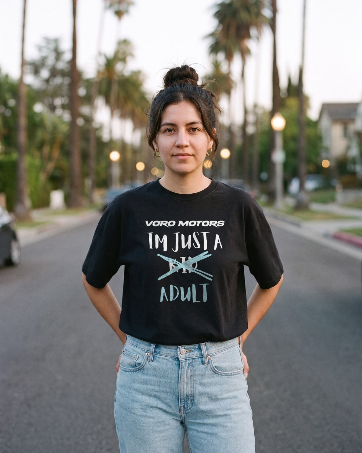 Woman in the I'm Just a Kid Adult tee on a palm-lined Silver Lake street at dusk