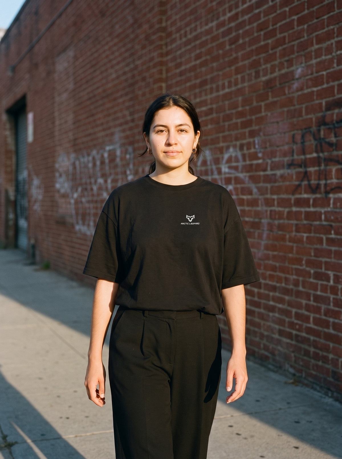 Arctic Leopard Logo Tee in black worn by a woman, Arctic Leopard logo printed on the left chest
