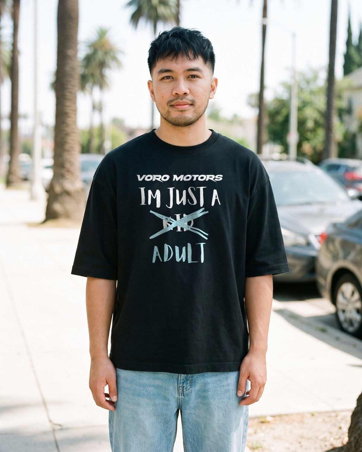 Man wearing the I'm Just a Kid Adult oversized tee in black on a palm-lined LA sidewalk