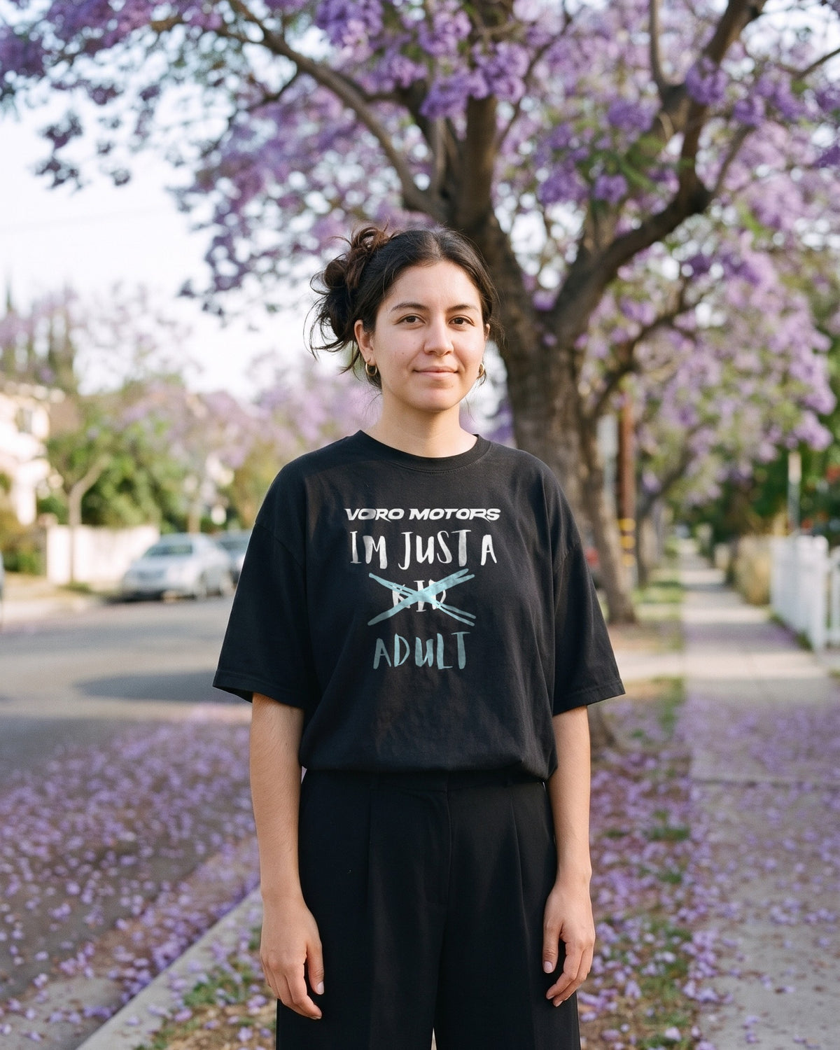 Woman in the I'm Just a Kid Adult oversized tee on a jacaranda-lined sidewalk