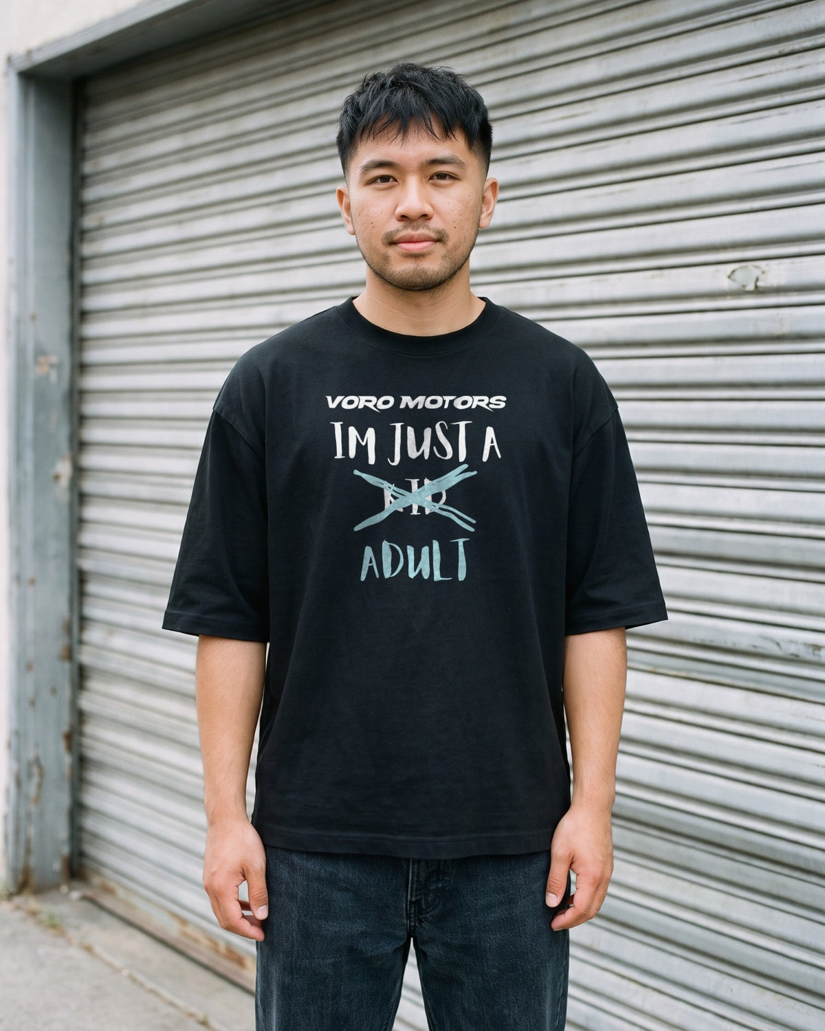 Man wearing the I'm Just a Kid Adult tee in black against a garage door in Highland Park, Los Angeles