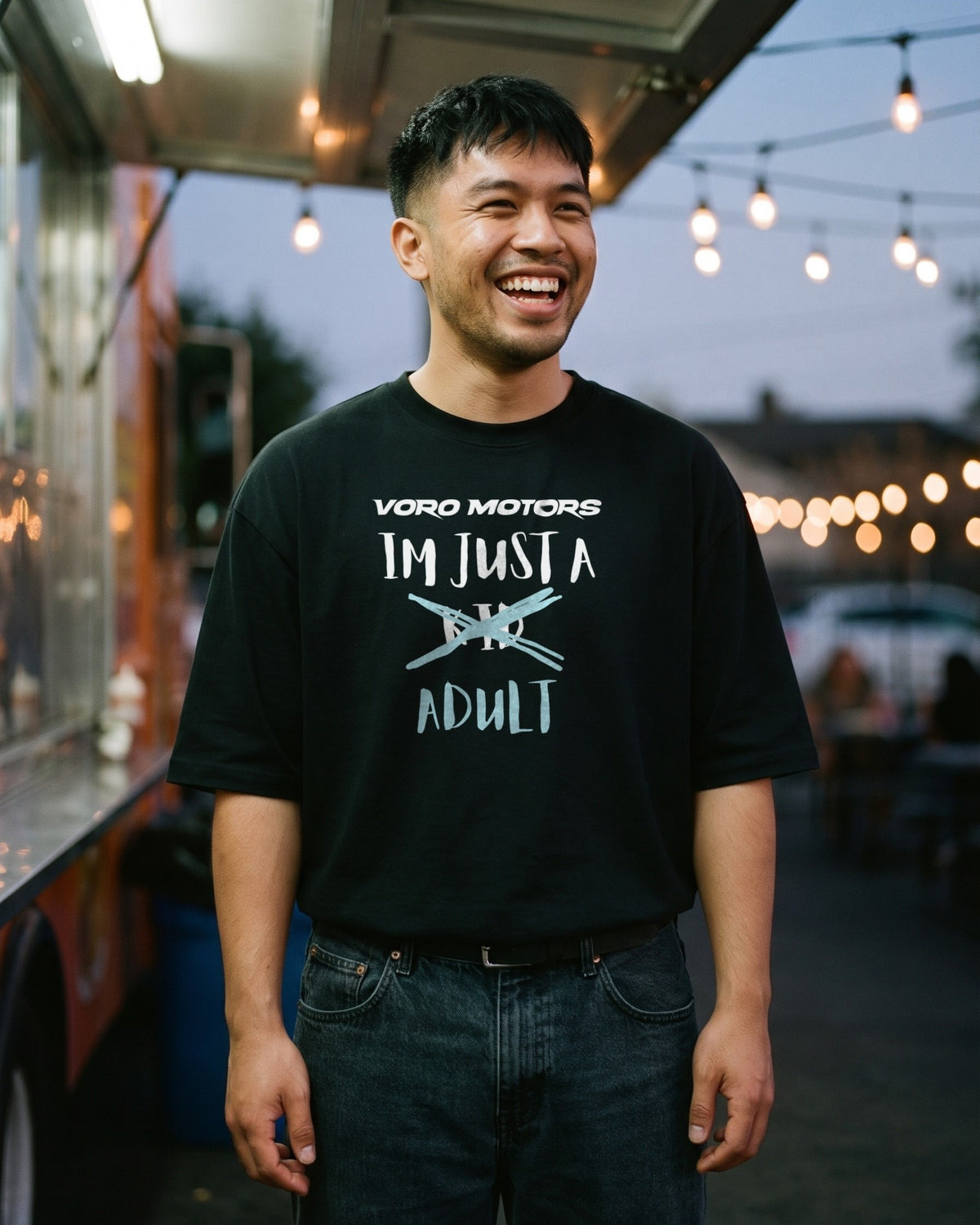 Man smiling in the I'm Just a Kid Adult tee at a taco truck at night in East LA