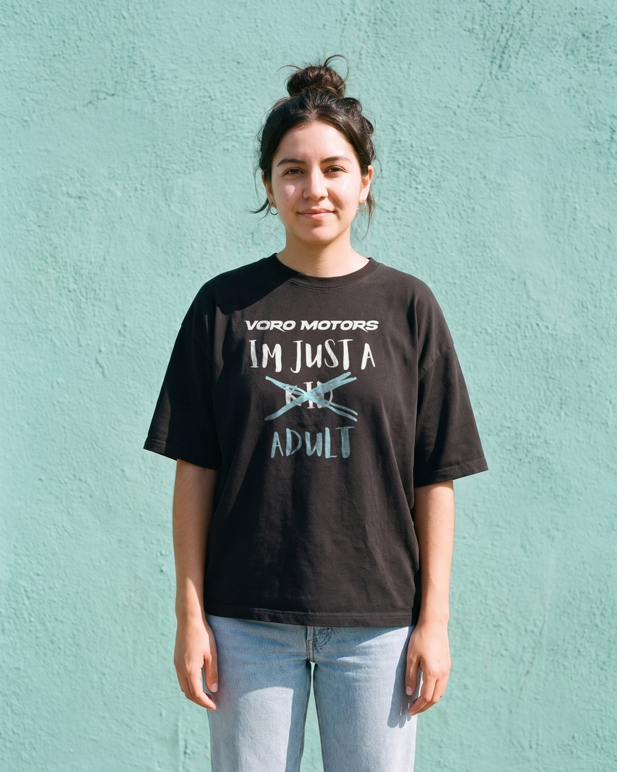 Woman wearing the I'm Just a Kid Adult tee in black against a teal wall in Echo Park, Los Angeles