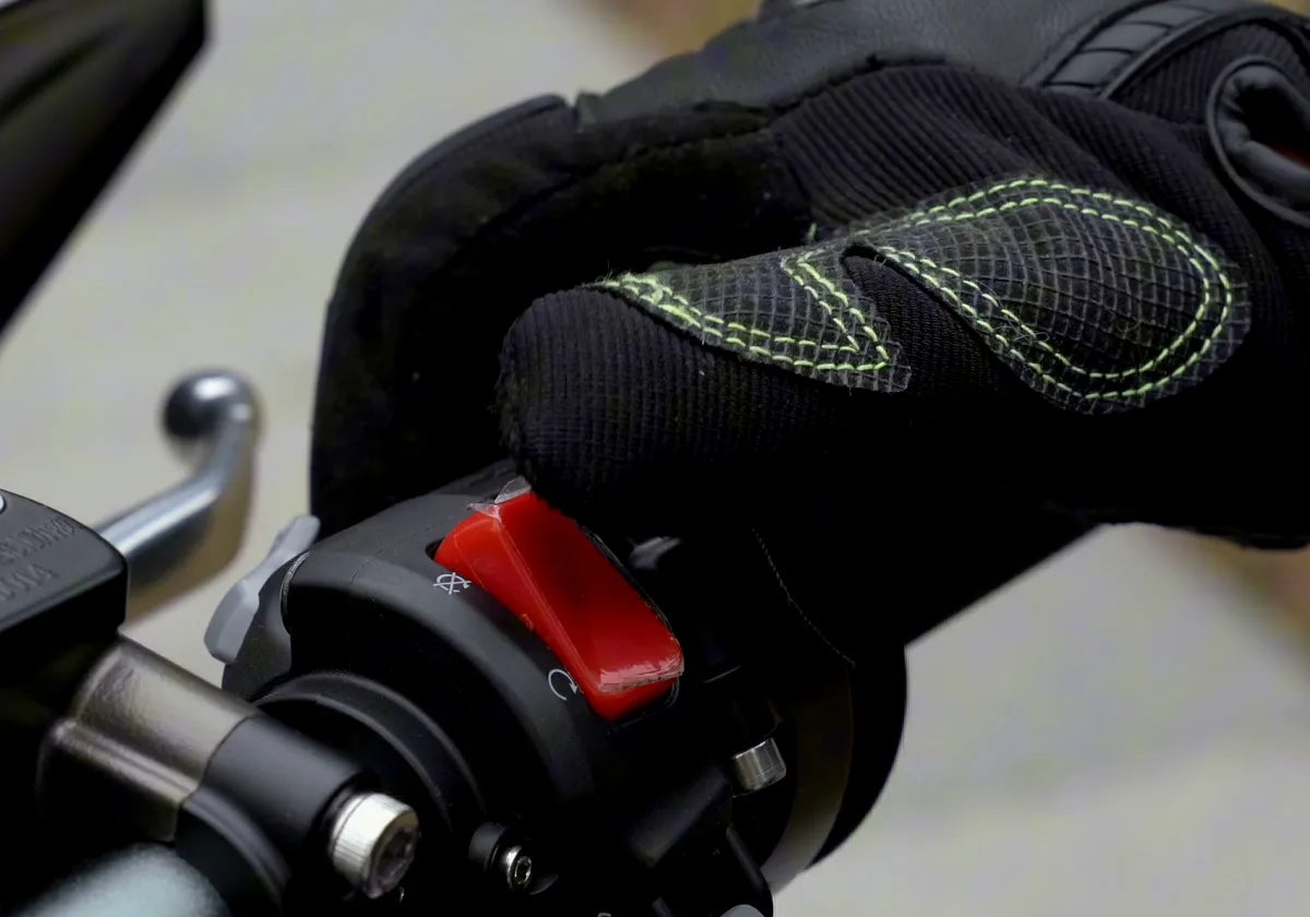 A gloved hand on the right bar of the Surron Ultra Bee, next to the red switch